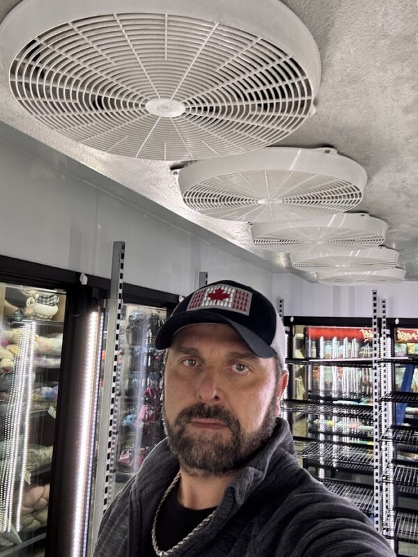 Refrigerated display aisle with ceiling-mounted fans and a person