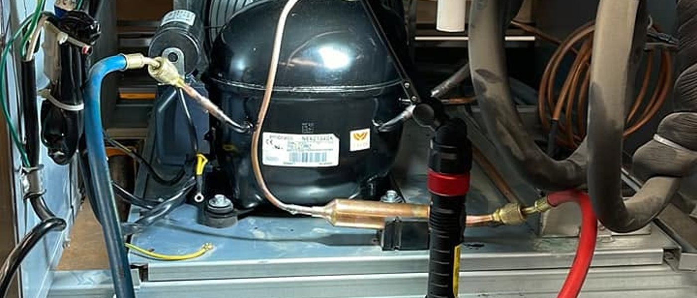 CooperFix technician charging an undercounter refrigeration unit with service hoses connected