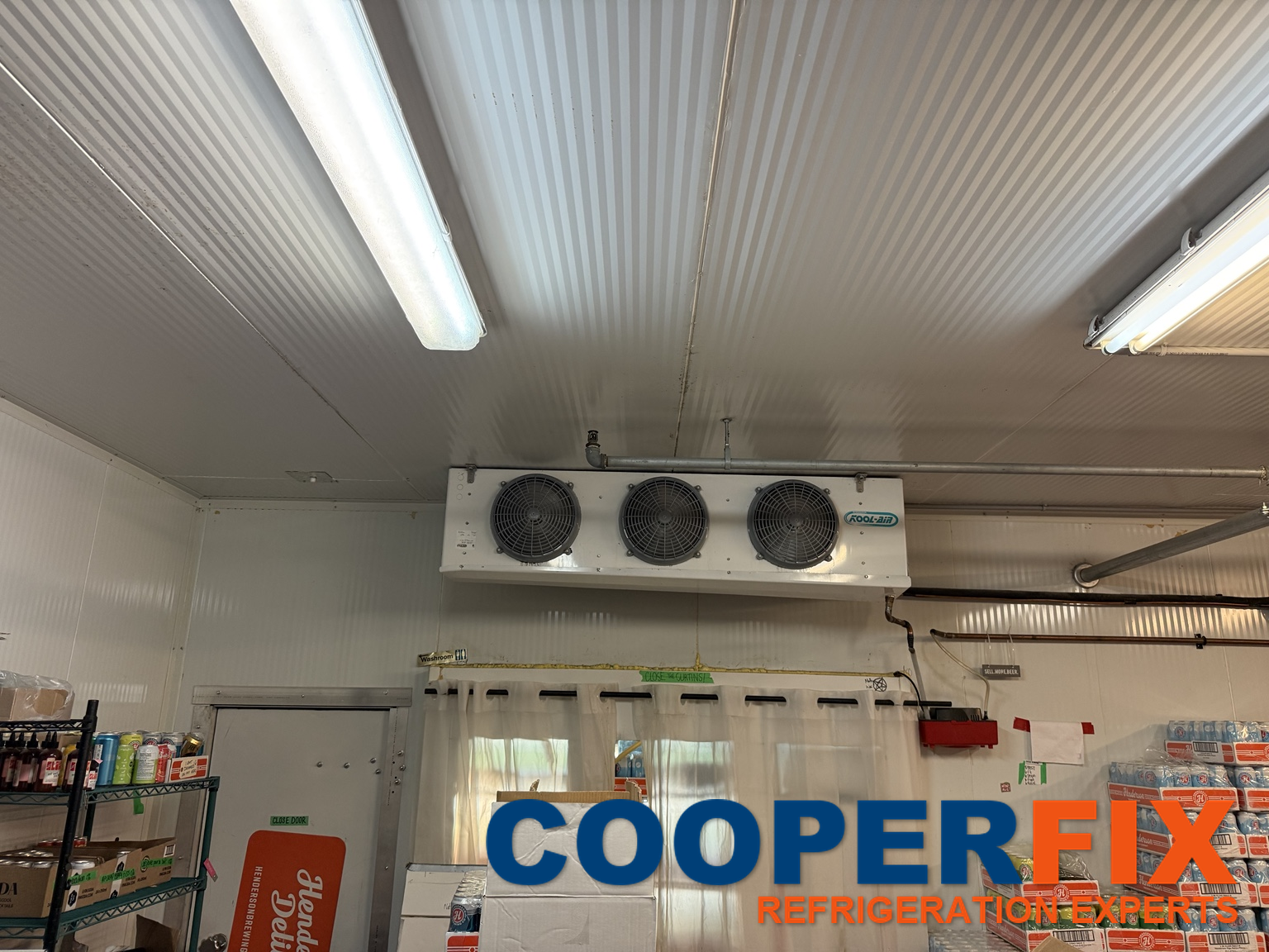 Three-fan evaporator mounted inside a cold room above strip curtains.