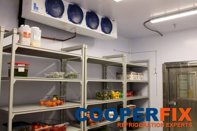 Four-fan evaporator above storage shelving inside a cold room.
