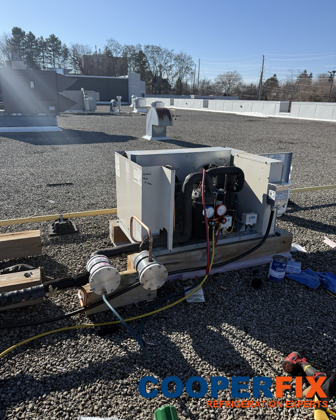 Commercial refrigeration condensing unit with service hoses on a rooftop.