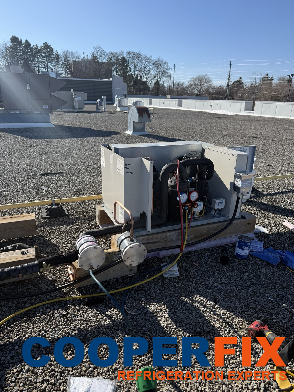 Open rooftop refrigeration condensing unit with service gauges and hoses.