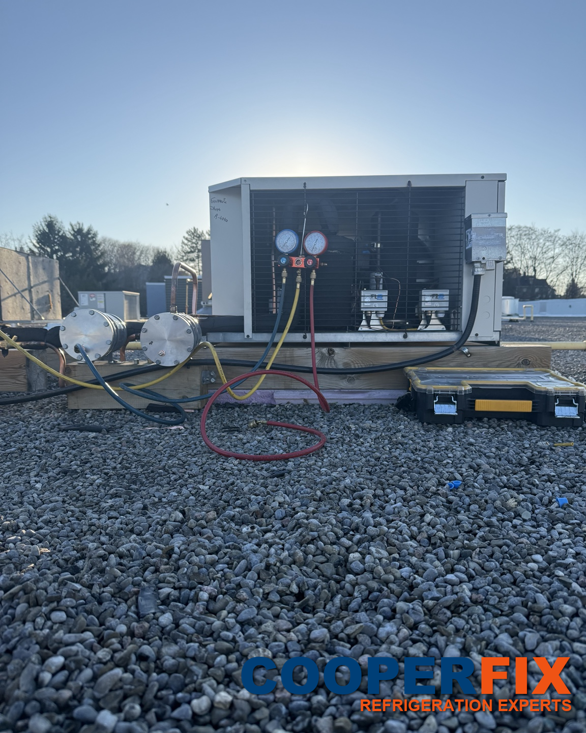 Commercial refrigeration condensing unit with service hoses on a rooftop.