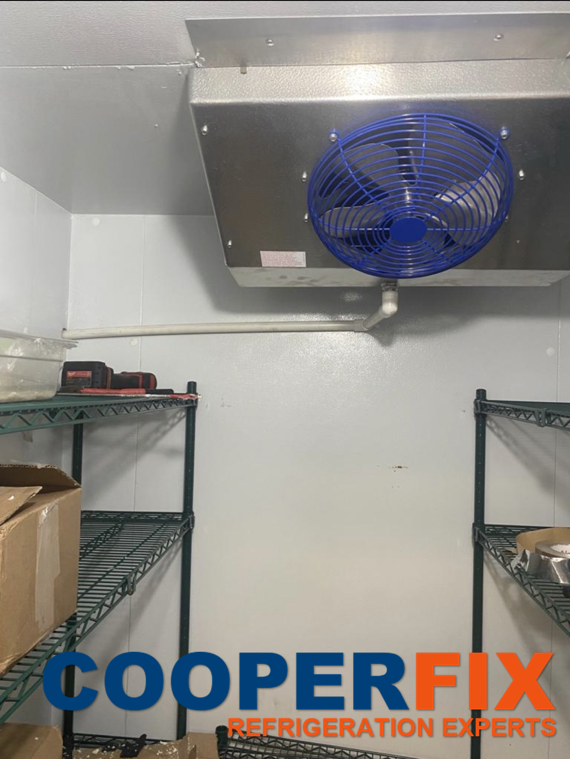 Single-fan cold-room evaporator with a blue fan guard above metal shelving.