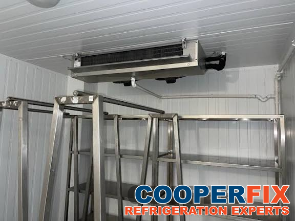 Commercial walk-in cold room with a ceiling evaporator above shelving.
