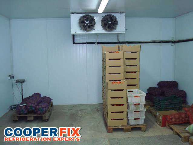 Twin-fan evaporator above boxes and bags of produce in a cold room.