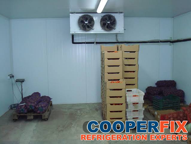 Twin-fan evaporator above boxes and bags of produce in a cold room.