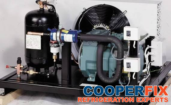 Refrigeration compressor assembly with a condenser fan, connected piping and visible control enclosures.